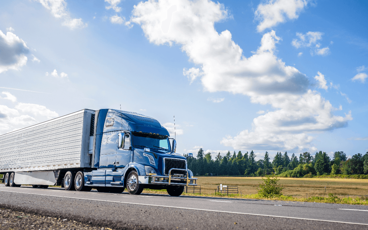 blue semi truck driving with a sunny sky