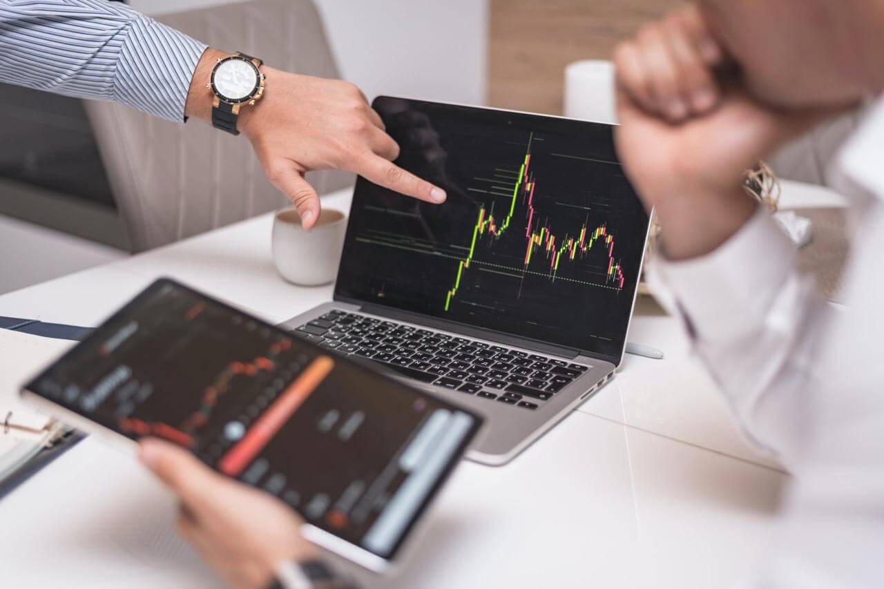 pointing at laptop with stock statistics and tablet with additional information