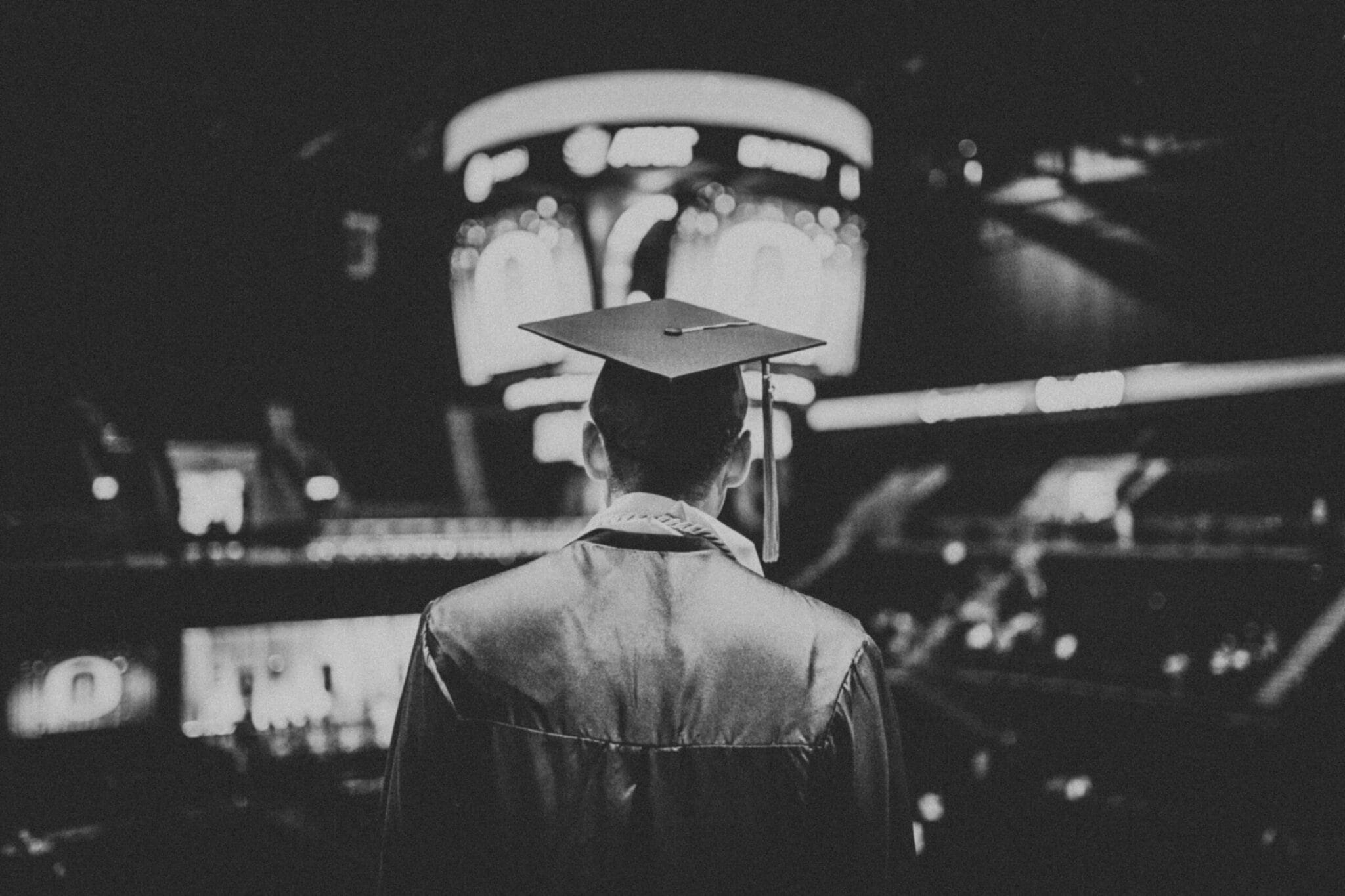 person in graduation gown looking at their graduates in a gymnasium