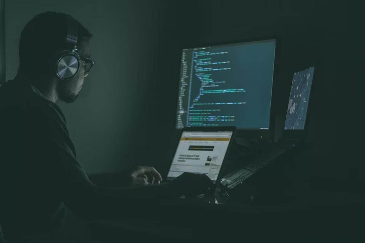 man in shadows on multiple computers