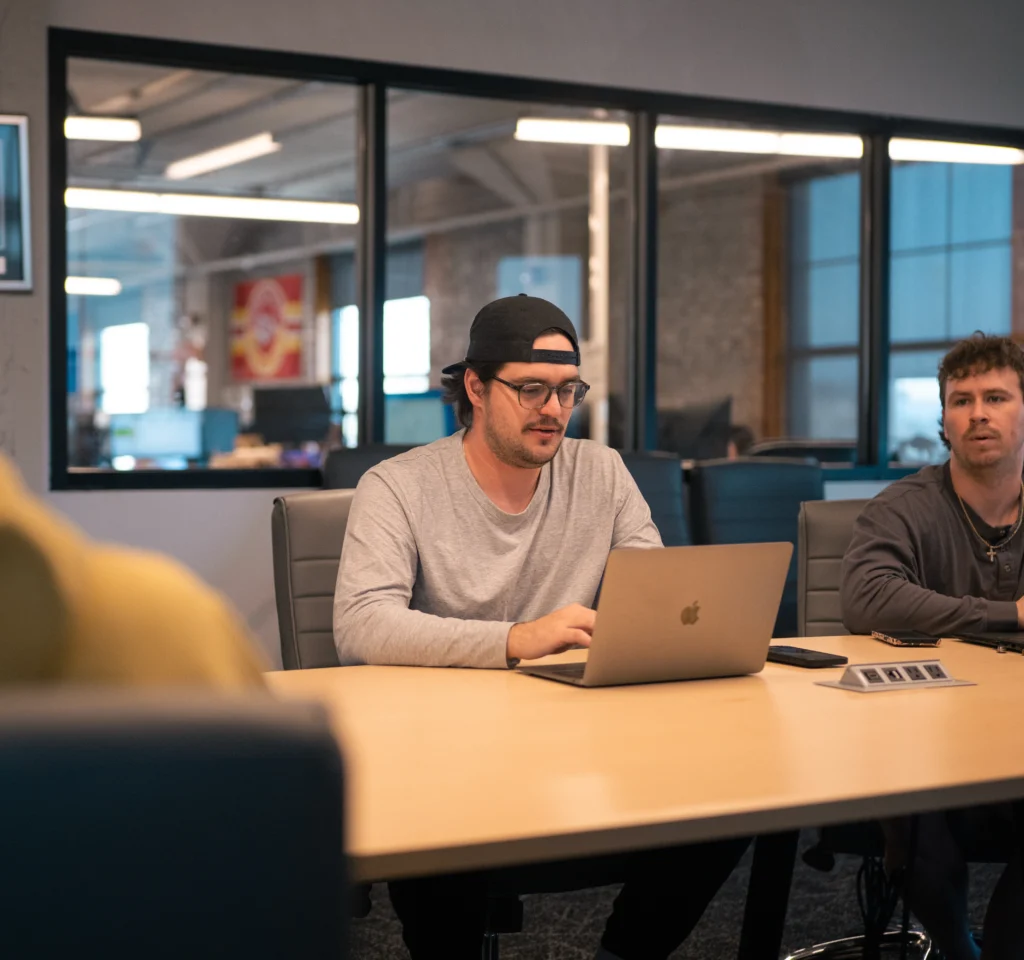 A freight operations specialist works on a laptop in a conference desk with other team members.