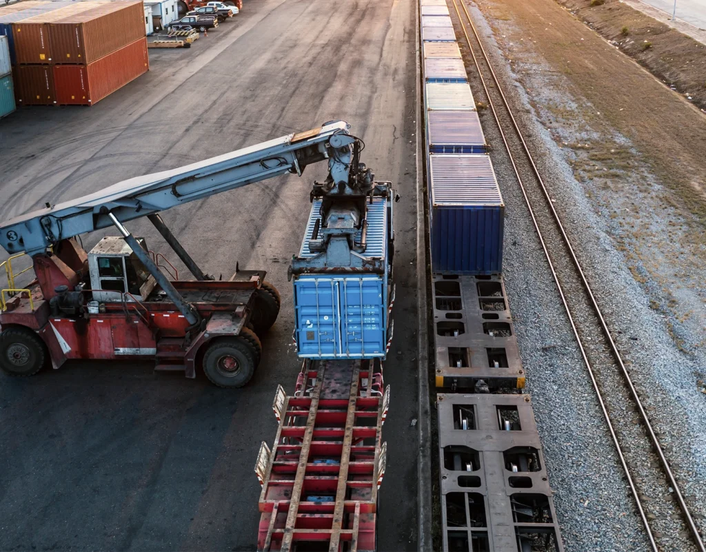 Equipment loads a container onto a train cart to be hauled via rail.