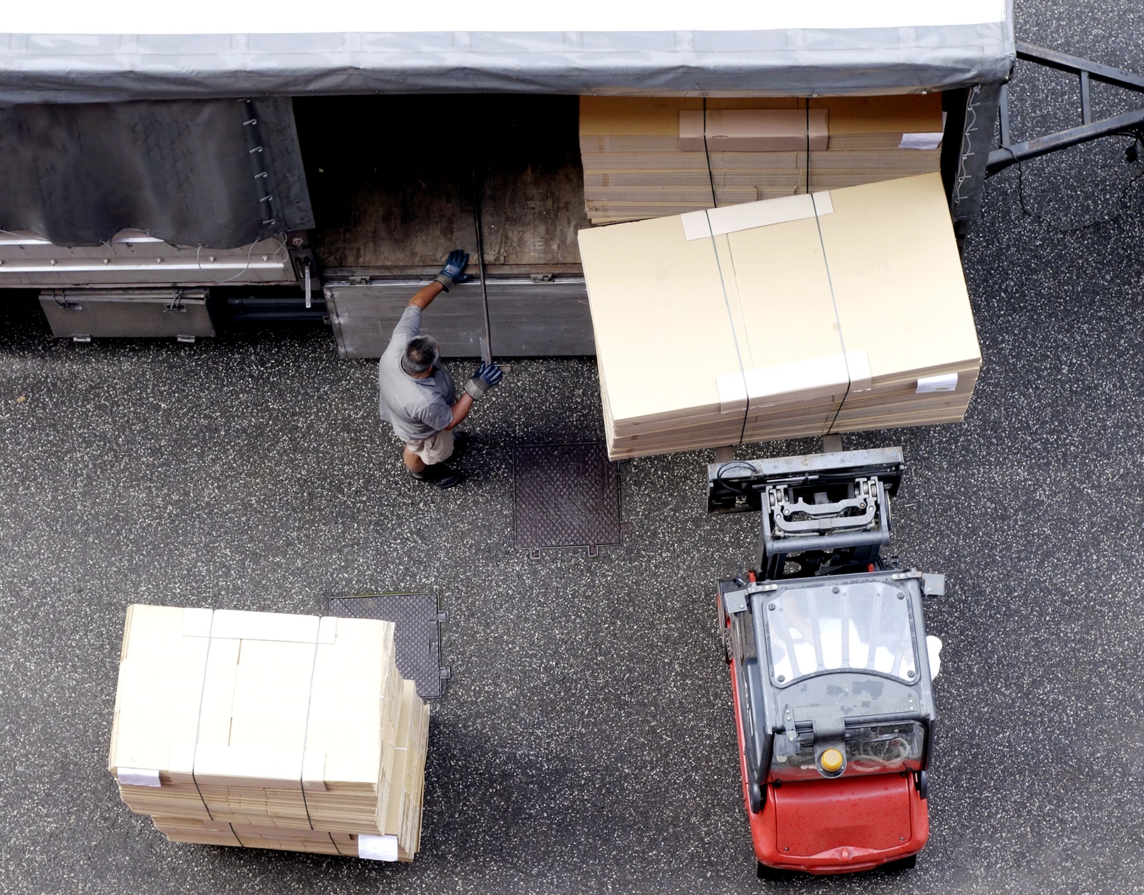 A man assists a forklift with loading boxed cargo into a the side of a truck.