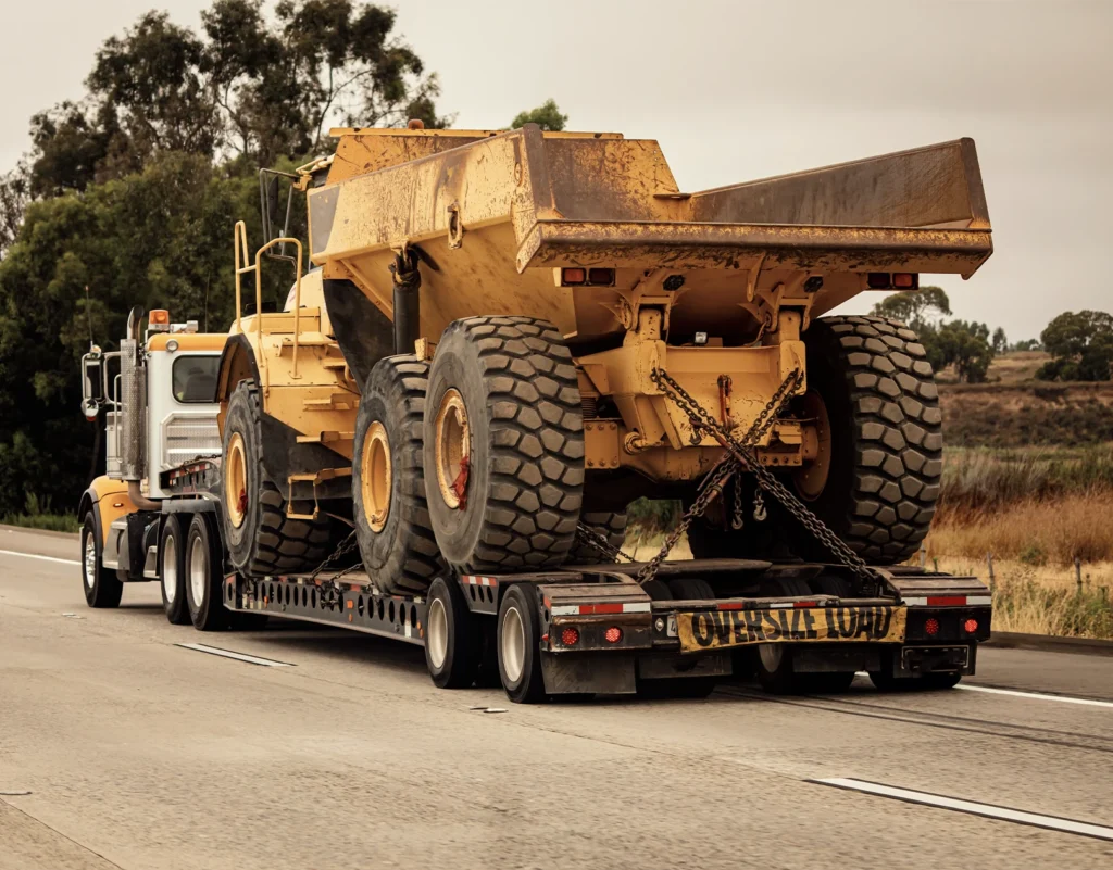 A flatbed truck hauls oversize construction equipment.