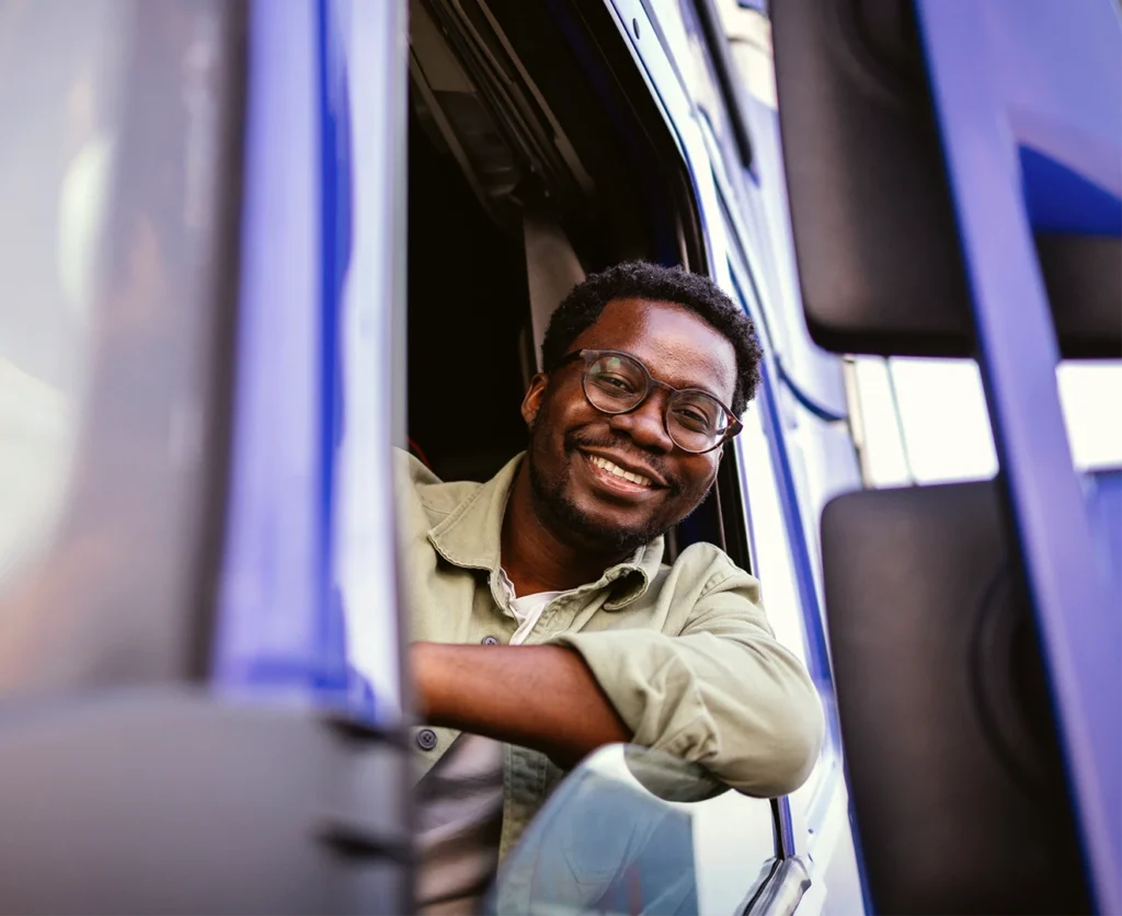 A happy truck driver leans out of his window to smile at the camera.