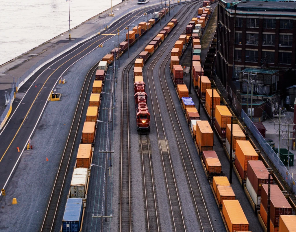 A train hauling cargo containers travels through rows of train cars sitting on the tracks.